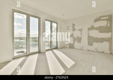 Sonnenlicht fällt durch große Fenster in einem leeren, unmöblierten Zimmer mit weißen Wänden im renovierten Apartment Stockfoto