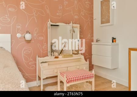 Stilvoller Spiegel mit Frisiertisch und Hocker an pfirsichfarbener Wand im modernen Schlafzimmer des modernen Hauses Stockfoto