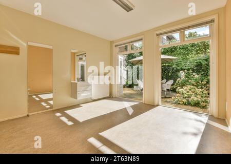 Sonnenlicht fällt auf den Boden in einem unmöblierten leeren Wohnzimmer durch große Fenster mit Blick auf üppige Pflanzen im Hinterhof Stockfoto