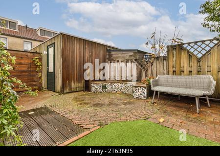 Holzschuppen und leere weiße Bank am Zaun in der gepflasterten Terrasse im Hinterhof vor bewölktem Himmel Stockfoto