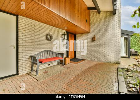 Terrasse mit leerer Bank vor dem modernen Wohngebäude mit Ziegelwänden und geschlossenen Türen während des Tages Stockfoto