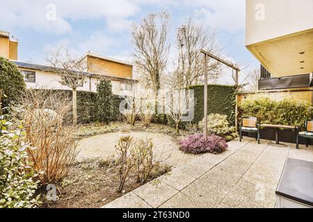 Stühle und Tisch auf der Terrasse mit einem kleinen Rasen mit Bäumen und Pflanzen, die im Hinterhof des Hauses gegen den Himmel wachsen Stockfoto