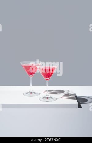 Gläser gefüllt mit roten Granatapfelcocktails vor gedämpftem grauen Hintergrund, die sanfte Schatten werfen Stockfoto