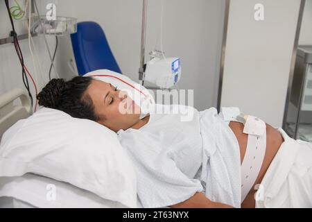 Nahaufnahme einer ruhigen schwangeren Frau, die in einem Krankenhausbett ruht und mit medizinischen Geräten verbunden ist und den Frieden und das Vertrauen in die Gesundheitsversorgung unterstreicht Stockfoto