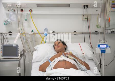 Eine schwangere Frau liegt in einem Krankenhausbett umgeben von medizinischen Geräten, was die Erwartung und medizinische Versorgung während der Schwangerschaft widerspiegelt Stockfoto