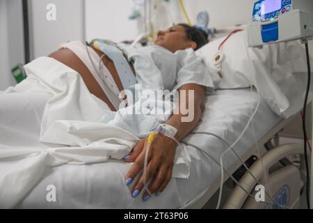 Eine schwangere Frau in einem Krankenhausbett, das mit medizinischen Geräten verbunden ist, zeigt die Ernsthaftigkeit und die Erwartung der Geburt Stockfoto