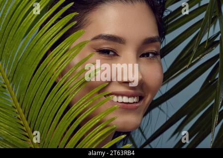 Verspieltes Mädchen guckt hinter Palmblättern hervor und lächelt. Stockfoto