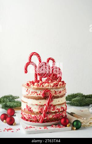 Mehrschichtiger Lebkuchenkuchen mit roten Lolli-Pops, farbigem Konfetti auf weißem Kuchenständer, Weihnachtskugeln, Tannenzweigen auf weißem Beton Stockfoto