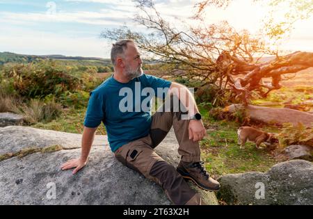 Ein glücklicher Rentner mit englischen Bulldoggen, die bei Sonnenuntergang im Peak District spazieren gehen. Hundetraining. Freizeit im Ruhestand Stockfoto