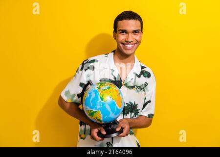 Foto von positivem nettem Kerl tragen trendiges Outfit Hände halten Globus Traum weltweite Reise Tour isoliert auf gelbem Hintergrund Stockfoto