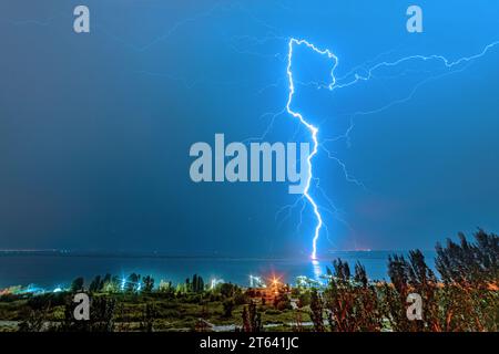 Nächtliche Blitze treffen auf den Pier am gegenüberliegenden Ufer des Flusses Stockfoto