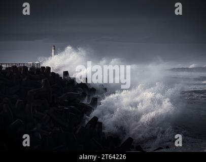Wellen stürmen bei Torness während des Sturms Babet gegen die Küste, mit dem Leuchtturm von Barns Ness im Hintergrund. Stockfoto