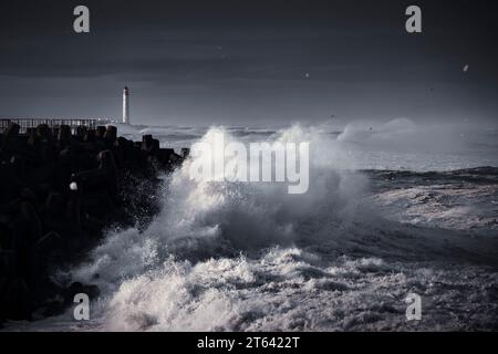 Wellen stürmen bei Torness während des Sturms Babet gegen die Küste, mit dem Leuchtturm von Barns Ness im Hintergrund. Stockfoto