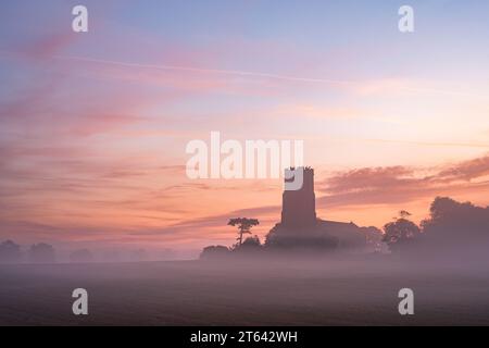 Ein roter Himmel bei Sonnenaufgang über der Kirche an einem nebeligen Sommermorgen. Stockfoto