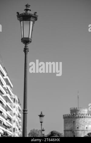 Blick auf eine Laterne, Wohngebäude und den berühmten Weißen Turm, auch bekannt als Lefkos Pyrgos in Thessaloniki, Griechenland, in Schwarz-weiß Stockfoto