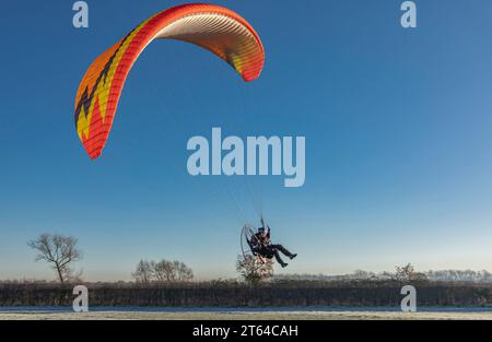 Männlicher Para-Gleiter landet auf einem eisigen Feld vor einem klaren, sehr blauen Himmel Stockfoto