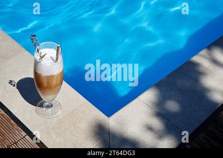 Eiskaffee mit Lavendel am Pool an einem heißen Sommertag. Das Foto wurde in einem hohen Winkel in der Nähe des blauen Wassers aufgenommen. Kopieren Sie den Bereich. Stockfoto