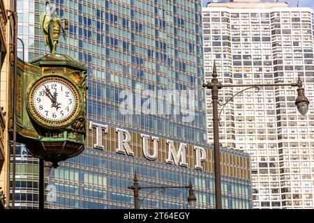 Die Uhr im Juweliergebäude wird kurz vor Hochmittags angezeigt. Im Hintergrund sehen Sie die Schrift Trump aus dem Trump Tower. Chicago, Usa. Trump Tower Chicago auf der DuSable Bridge und gegenüber einer alten Straßenuhr mit der Zeitanzeige „fünf bis zwölf“ Stockfoto