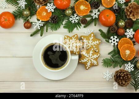 Tasse Kaffee auf dem weißen hölzernen Winterhintergrund mit weihnachtsdekorationen, Mandarinen, Kegeln, Lebkuchen und Kopierraum Stockfoto