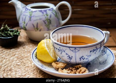 Morgens auf Holztisch am Balkon, Zeitungen, Tasse Naturtee, Teekanne, Bio-Honig vom Bauernhof, frische grüne Teeblätter und Bio-Früchte Stockfoto
