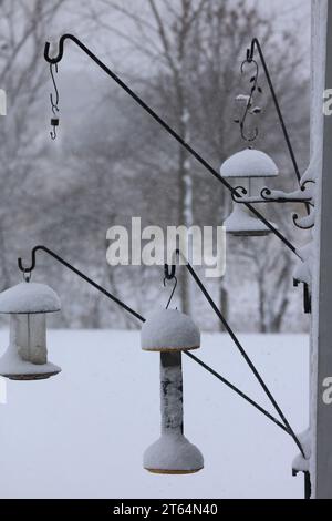 Drei Vogelfuttergeräte hängen an schwarzen Eisenhaken, die an einem Holzspalier befestigt sind und während eines Schneesturms in Wisconsin mit mehreren Zentimetern Schnee bedeckt waren Stockfoto