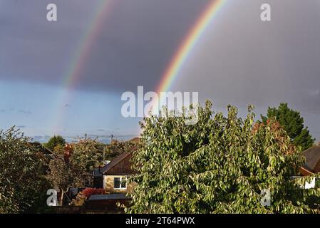Regenbogen bildet sich vor einem grauen Himmel mit Baumkronen im Vordergrund Stockfoto