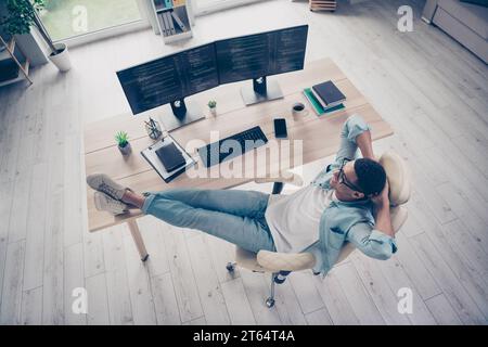 Ganzkörperfoto obere Ansicht des jungen positiven Mannes, der sich entspannt, hat erfolgreich die Programmierung von Code-Software-Beinen auf dem Schreibtisch im Büroarbeitsplatz abgeschlossen Stockfoto