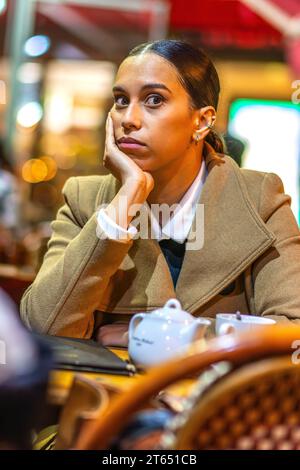 Eine junge Frau, die mit viel Aufmerksamkeit anstarrt und sich Kopf auf Hand an den Kaffeetisch mit Tee ausruht - Paris, Frankreich. Stockfoto