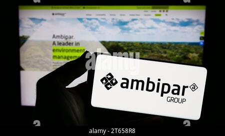 Person mit Smartphone und Logo des brasilianischen Umweltdienstleisters Ambipar Group vor der Website. Schwerpunkt auf dem Display des Telefons. Stockfoto