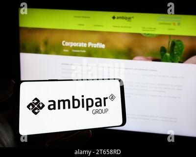 Person, die ein Mobiltelefon mit dem Logo des brasilianischen Umweltdienstleisters Ambipar Group vor der Webseite hält. Schwerpunkt auf dem Display des Telefons. Stockfoto