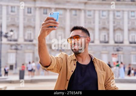 Glücklicher Mann, der Selfie macht, der auf der Straße der Stadt spaziert, lächelnder Kerl, der draußen in die Kamera schaut Stockfoto