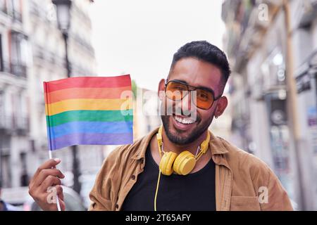 Hiispanischer Mann mit Bart und Sonnenbrille hebt eine lgtbi-Flagge. Stockfoto