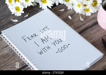 Fürchte nicht, dass ich bei dir bin, Gott. Handgeschriebener Text im Notizbuch mit Blumen und Kaffeetasse auf Holz. Inspirierende Bibelverse. Frieden und Liebe christliches Konzept. Stockfoto