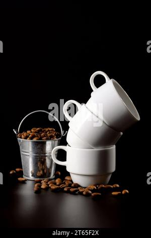 Geröstete Kaffeebohnen und weiße Kaffeetassen auf schwarzem Hintergrund. Vertikales Bild Stockfoto