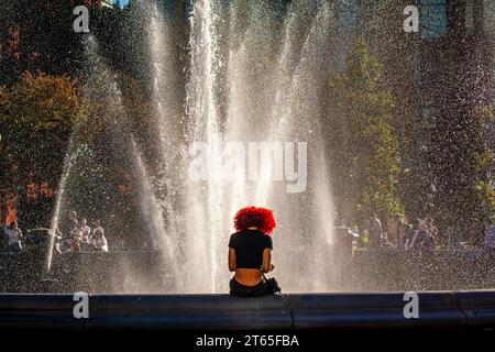 Eine junge schwarze Frau mit rotem Haar sitzt am Brunnen im Washington Square Park, Manhattan, New York City Stockfoto