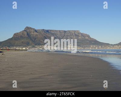 Weitwinkelaufnahme eines leeren Sandstrands und hereinbrechender Meereswellen mit dem ikonischen Tafelberg im Hintergrund in Kapstadt, Südafrika Stockfoto