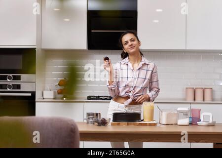 Hübsche Frau, die Pflaumenkuchen in heller, moderner Küche kocht. Genießen Sie die Zubereitung von hausgemachten Speisen Stockfoto