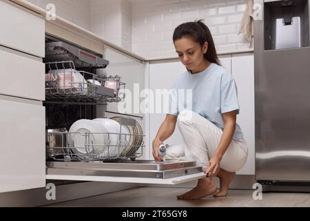 Frau gießt Spülmittel in das Geschirrspülfach in der modernen weißen Küche Stockfoto