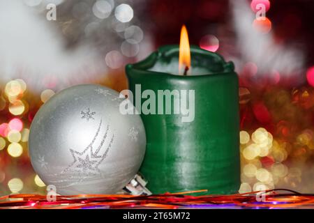 Weihnachtsszene aus silberner Kugel und brennende Kerze gegen verschwommen Hintergrund Stockfoto