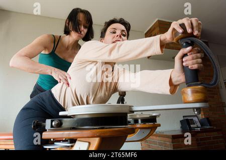 Kaukasische Erwachsene Rehabilitationslehrerin korrigiert die Rückenhaltung ihrer Schülerin während des Trainings auf gyrotonic-Trainingsgerät, Copy sp Stockfoto