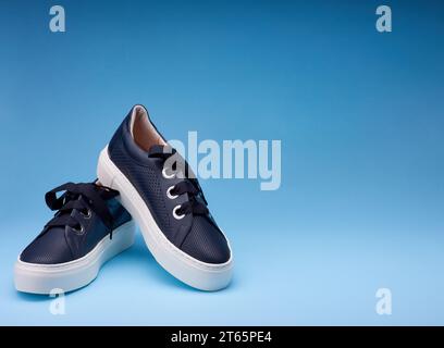 Ein Paar marineblauer perforierter Leder-Sneaker mit dicker weißer Plaform und dicker Schnürsenkel isoliert auf dem blauen Farbverlauf Hintergrund mit Kopierraum f Stockfoto