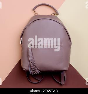 Moderner brauner Lederrucksack für Damen mit Griff und Reißverschlusstasche mit Quastenzug auf kreativem mehrfarbigem Hintergrund. Elegantes f Stockfoto