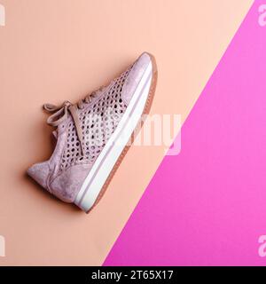 Modischer Damen-Sneaker aus staubrosafarbenem Leder mit Perforation und glänzendem Effekt und weiß-rosa-brauner Sohle auf einem pfirsichrosa Kontraststreifen Stockfoto