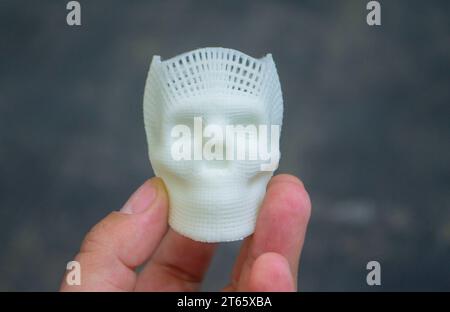 Person mit Fingern der Hand kleiner Prototyp eines menschlichen Schädels in 3D gedruckt aus geschmolzenem weißem Kunststoff. Dreidimensionales Modell. Additive progressive Medizintechnik. Moderne neue Druckindustrie. Stockfoto