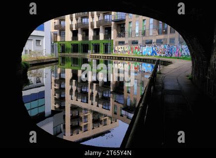 Eine gekrümmte Backsteinbrücke über den Regents Canal an der Camden Road mit Gebäuden und nahezu perfekten Reflexionen in Camden Town, London, England Stockfoto