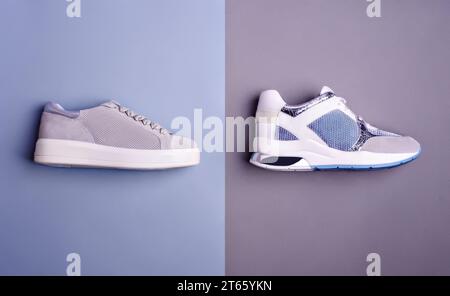 Seitenansicht zweier trendiger Sneakers in grauen, weißen und blauen Farben, isoliert auf zweifarbigem blaugrauem Hintergrund. Draufsicht, flach. Kreativ Stockfoto