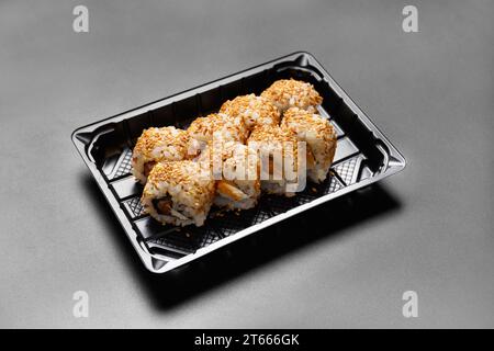 Sushi-Brötchen mit Lachs in einer Plastikverpackung, auf schwarzem Hintergrund, Draufsicht. Lieferung von Sushi, Brötchen zum Mitnehmen. Stockfoto