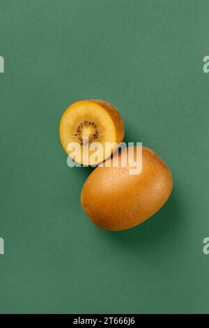 Ganze und halbierte reife goldene Kiwi, isoliert auf grünem Hintergrund. Kiwi mit gelb saftigem süßem Fruchtfleisch (Actinidia chinensis). Stockfoto