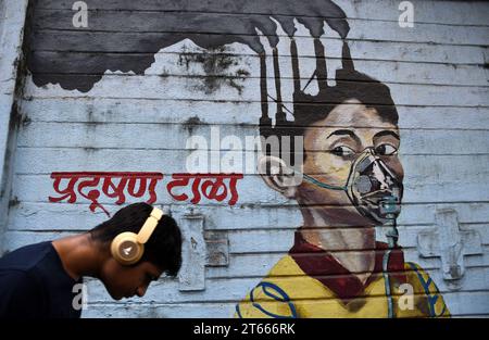 Mumbai, Maharashtra, Indien. November 2023. Ein Mann mit Kopfhörern geht an einem Wandgemälde vorbei, um ein Bewusstsein für die Luftverschmutzung in Mumbai zu schaffen. Die Luftverschmutzung in Mumbai erreicht aufgrund der laufenden Bauarbeiten an mehr als sechstausend Standorten, einschließlich Infrastrukturprojekten, bei denen Staub in der Luft schwebt, ein alarmierendes Niveau. es vermischt sich mit dem Fahrzeugrauch und anderen chemischen Stoffen, die in der Luft schwebt, um Smog zu erzeugen, der für die Gesundheit der Bürger schädlich ist. (Credit Image: © Ashish Vaishnav/SOPA Images via ZUMA Press Wire) NUR REDAKTIONELLE VERWENDUNG! Nicht für kommerzielle USA Stockfoto