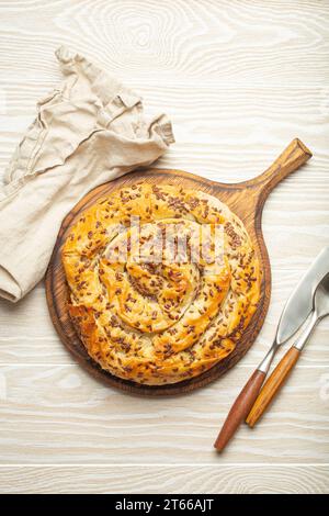 Bürek aus Filoteig mit Füllung auf Schneidebrett, weißer hölzerner rustikaler Hintergrund von oben. Traditioneller herzhafter Spiralkuchen aus dem Balkan, Mitte Stockfoto